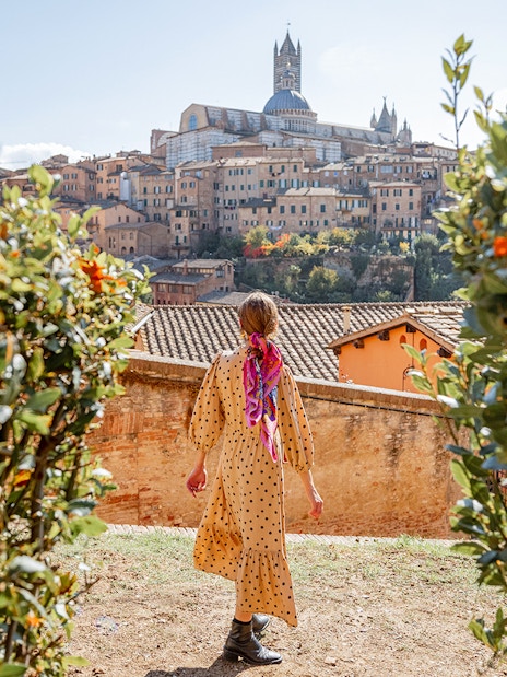 Person walking towards Siena Cathedral in Tuscany, Italy, surrounded by greenery.