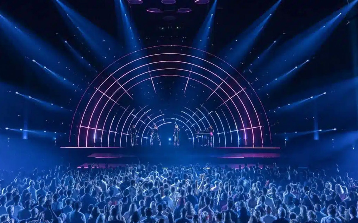 Crowd watching ABBA Voyage concert with illuminated stage and performers.