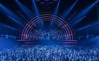 Crowd watching ABBA Voyage concert with illuminated stage and performers.