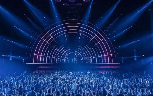 Crowd watching ABBA Voyage concert with illuminated stage and performers.