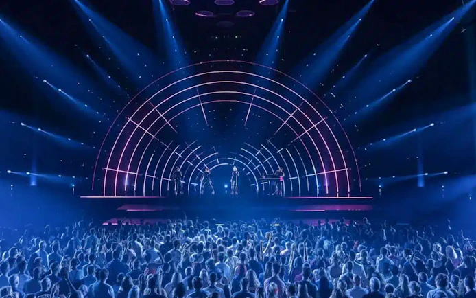 Crowd watching ABBA Voyage concert with illuminated stage and performers.
