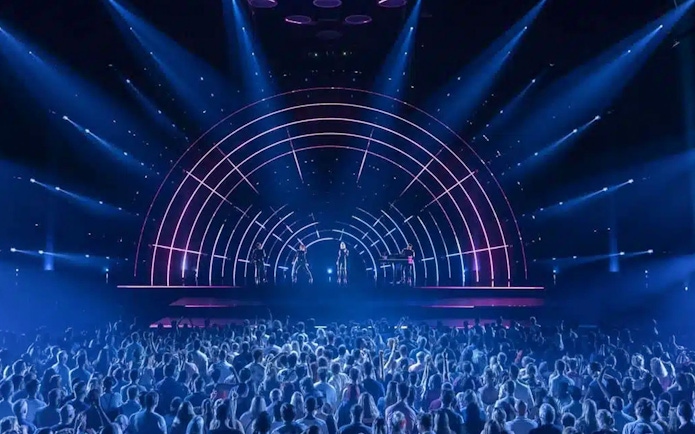 Crowd watching ABBA Voyage concert with illuminated stage and performers.