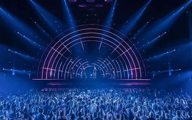 Crowd watching ABBA Voyage concert with illuminated stage and performers.