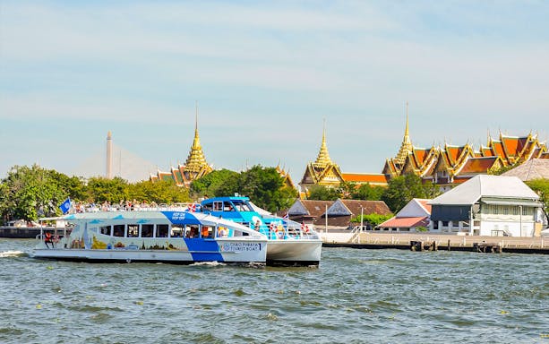 Tourist boat on Chao Phraya River with Bangkok temples in the background.