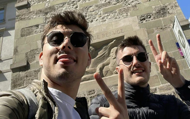 Two people posing with peace signs in front of a historic stone relief in Geneva.