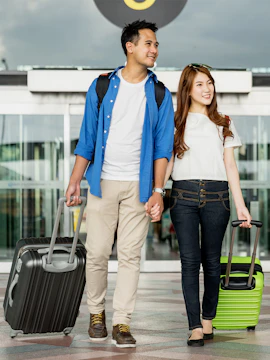 Couple with luggage at Malaysia airport entrance for transfer and SIM card service.