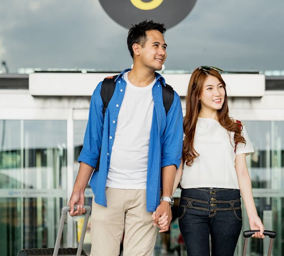 Couple with luggage at Malaysia airport entrance for transfer and SIM card service.