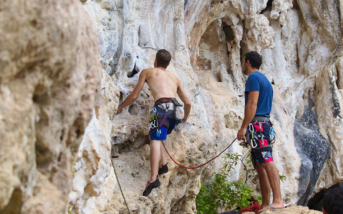 Rock climbers scaling limestone cliffs at Railay Beach, Krabi during a climbing course.