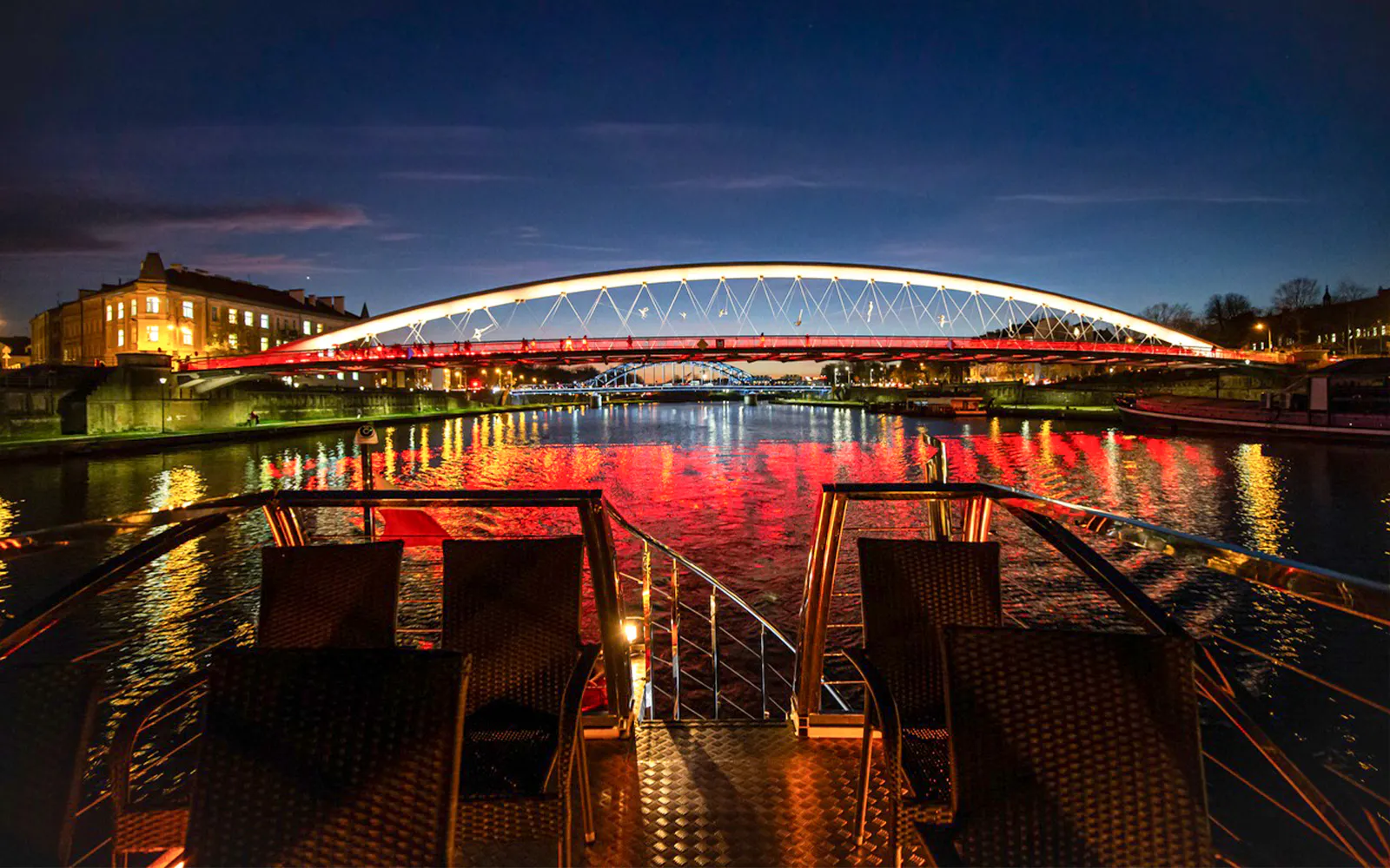 Catamaran view of illuminated bridge over Vistula River at night in Krakow.