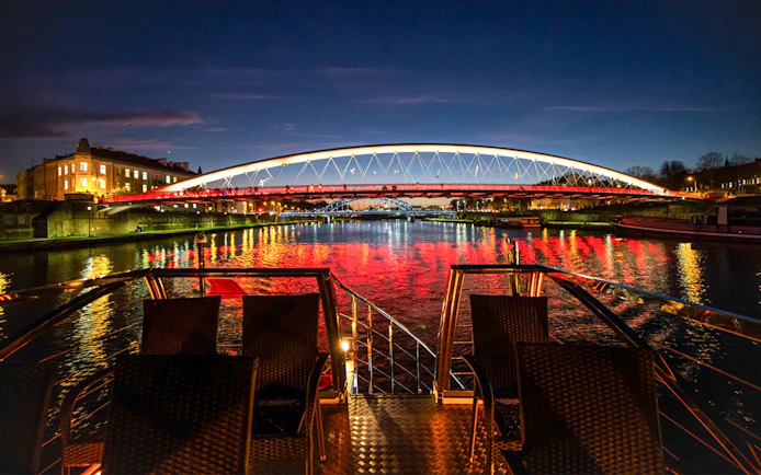 Catamaran view of illuminated bridge over Vistula River at night in Krakow.