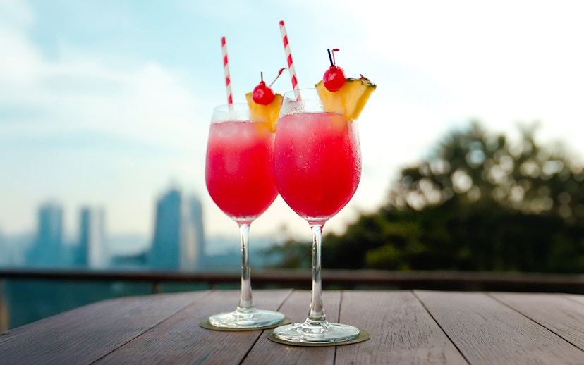 Two tropical cocktails on a table with a view of Singapore skyline.