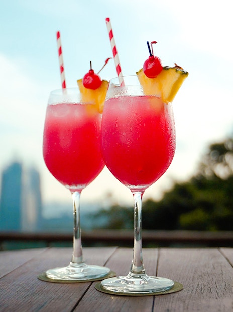 Two tropical cocktails on a table with a view of Singapore skyline.