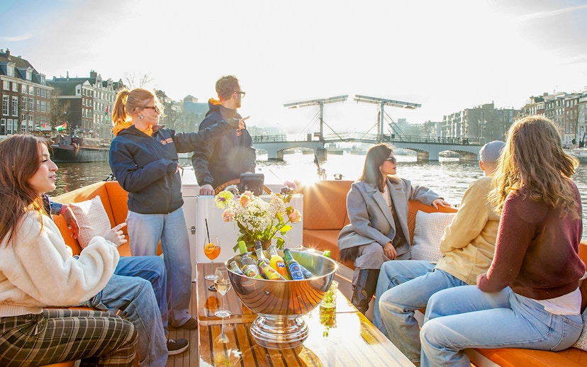 Guests enjoying an open boat cruise on Amsterdam canal with view of the Skinny Bridge.