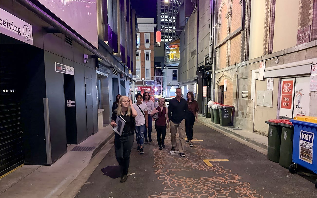 Group walking through a dimly lit alley in Brisbane on a true crime tour.