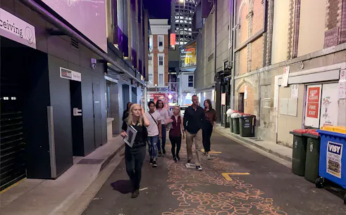 Group walking through a dimly lit alley in Brisbane on a true crime tour.