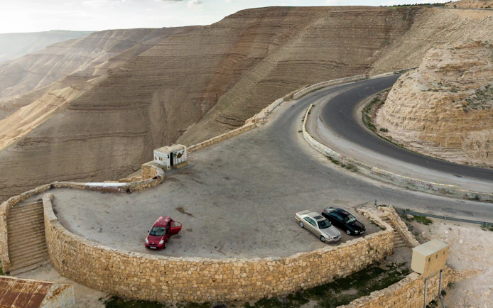 Aerial view of King Highway near Wadi Mujib Reservoir with parked cars and winding road.