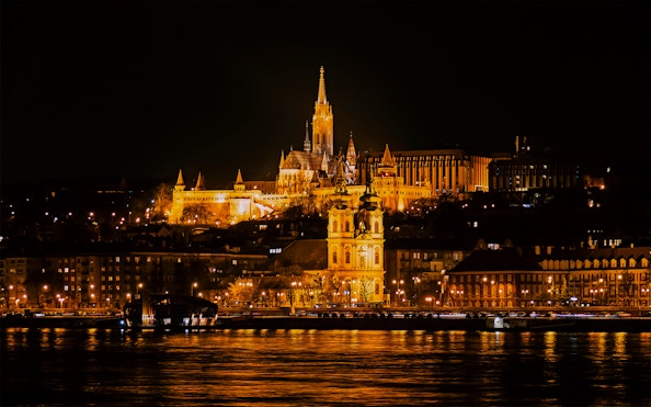 Matthias Church illuminated at night from a Danube River cruise in Budapest.
