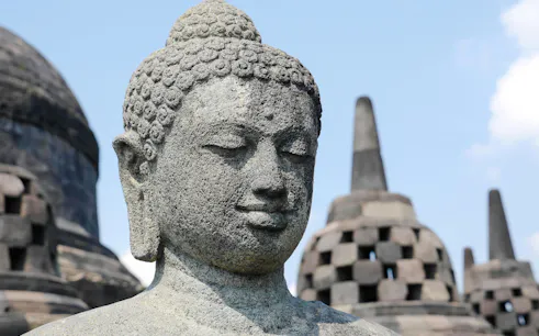 Buddha statue at Borobudur Temple, Yogyakarta, with stupas in the background.