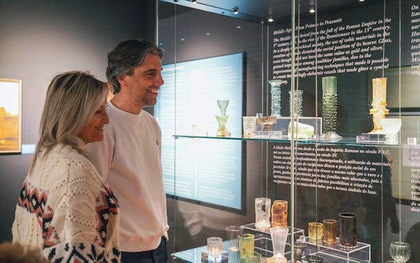 Visitors admiring glass artifacts at The Bridge Collection exhibit.