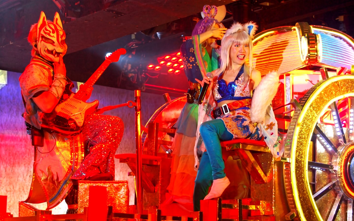 Performers in vibrant costumes with a samurai mask and guitar at a Tokyo cultural show.