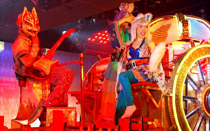 Performers in vibrant costumes with a samurai mask and guitar at a Tokyo cultural show.