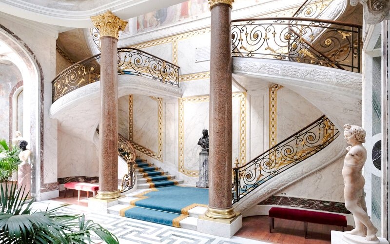Jacquemart André Museum grand staircase with ornate railings and classical sculptures.