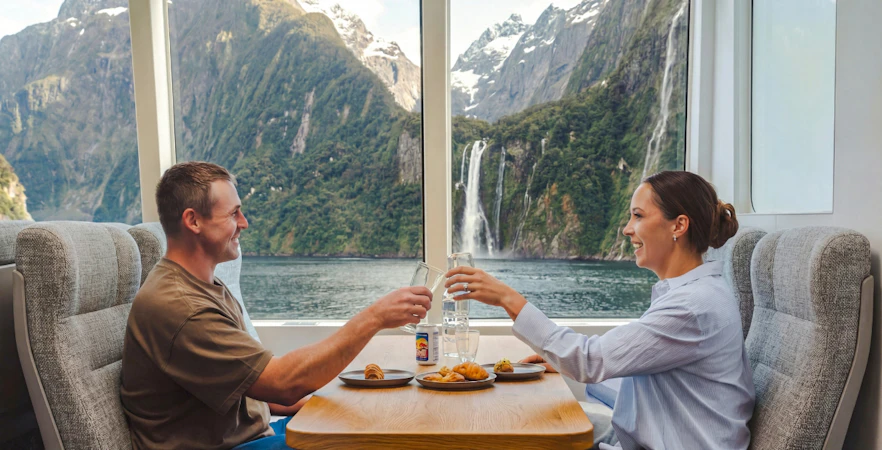 Couple enjoying a meal with a view of Milford Sound waterfall on a VIP cruise from Te Anau.
