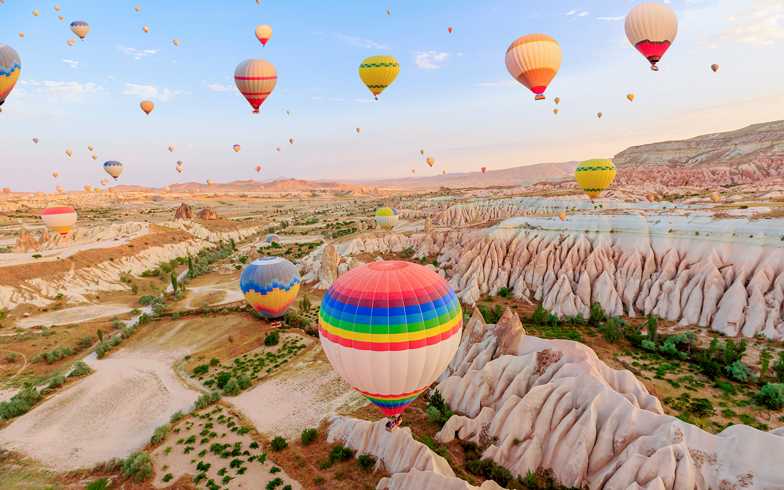 Hot air balloons over Goreme Rose Valley, Cappadocia, with unique rock formations.