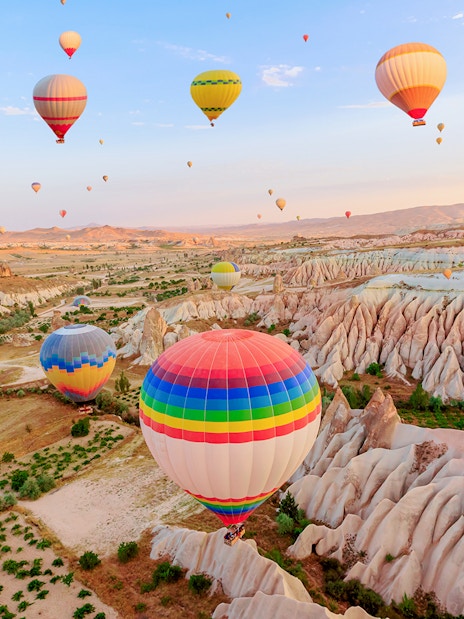 Hot air balloons over Goreme Rose Valley, Cappadocia, with unique rock formations.