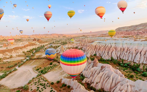 Hot air balloons over Goreme Rose Valley, Cappadocia, with unique rock formations.