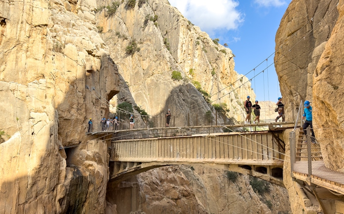 Hikers crossing suspension bridge on Caminito del Rey guided tour in Spain.