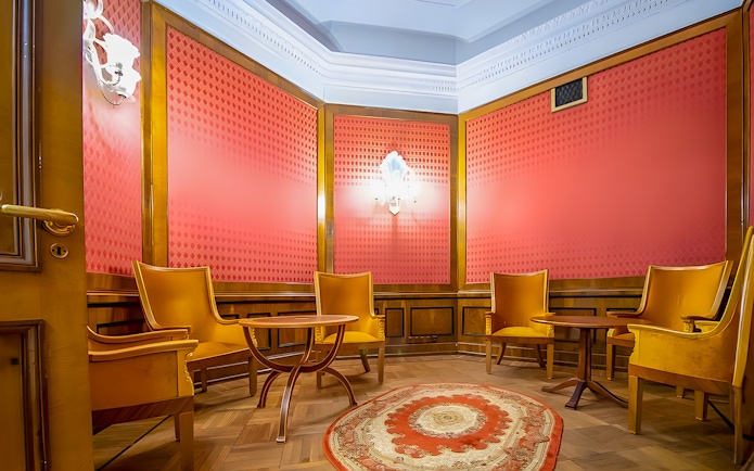 Meeting room with wooden chairs and table, red walls, and ornate rug at Palace of Culture and Science.