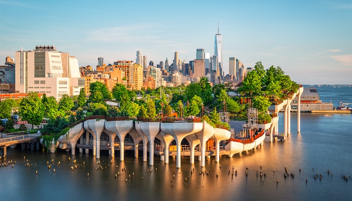 Tourists enjoying a sunny day at Little Island, New York, with the city skyline in the background