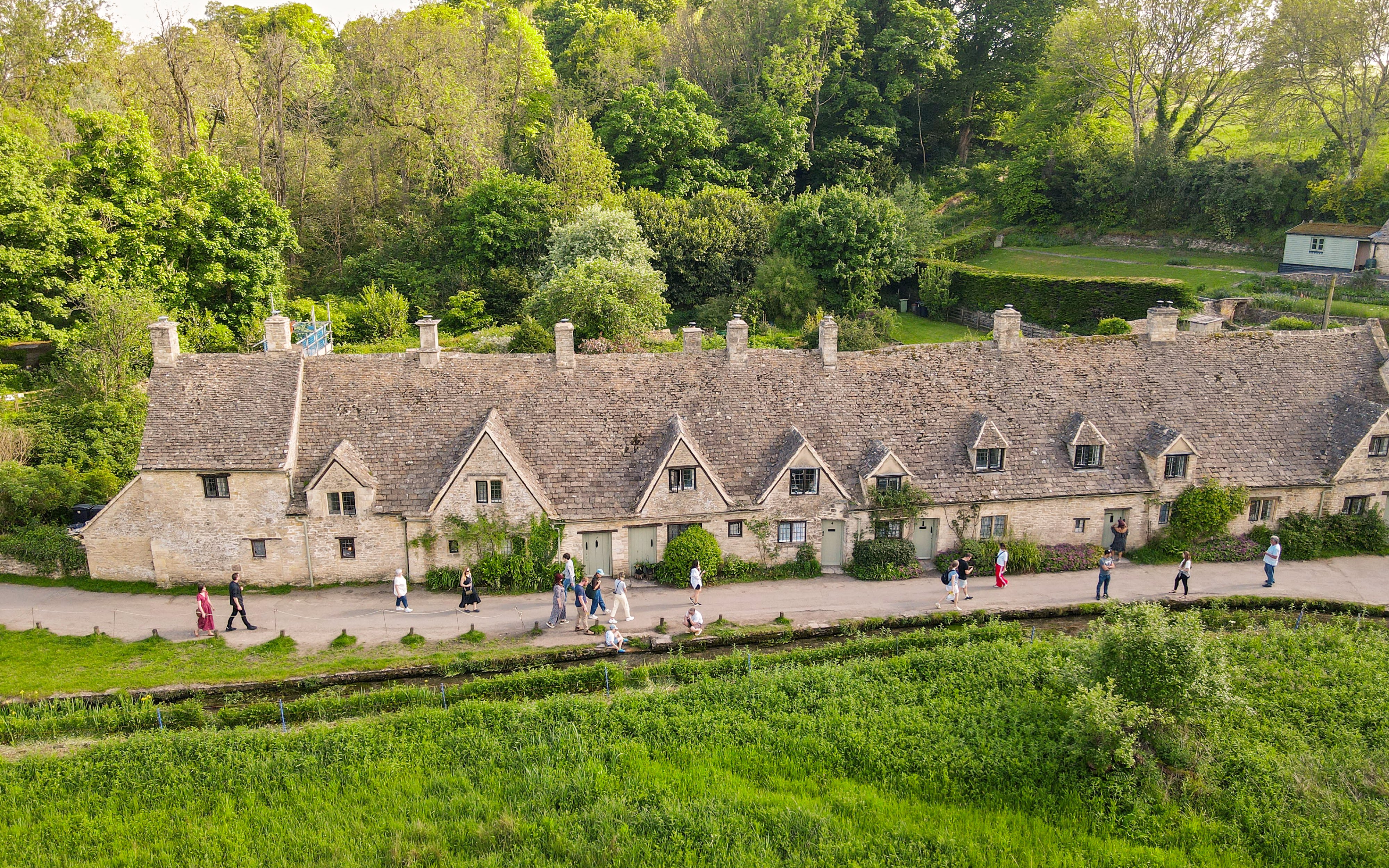 Row of historic stone cottages in Cotswold with tourists walking along the path.