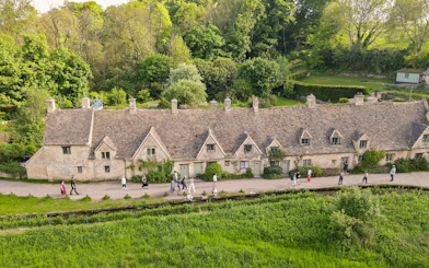 Row of historic stone cottages in Cotswold with tourists walking along the path.