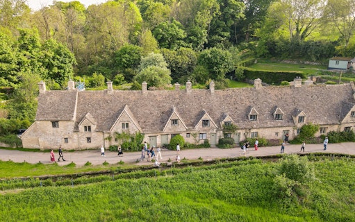 Row of historic stone cottages in Cotswold with tourists walking along the path.