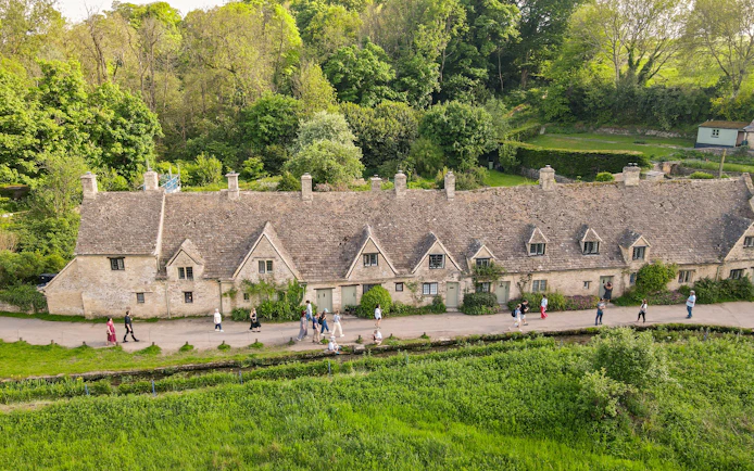 Row of historic stone cottages in Cotswold with tourists walking along the path.