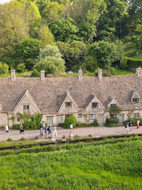 Row of historic stone cottages in Cotswold with tourists walking along the path.