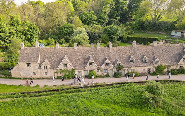 Row of historic stone cottages in Cotswold with tourists walking along the path.