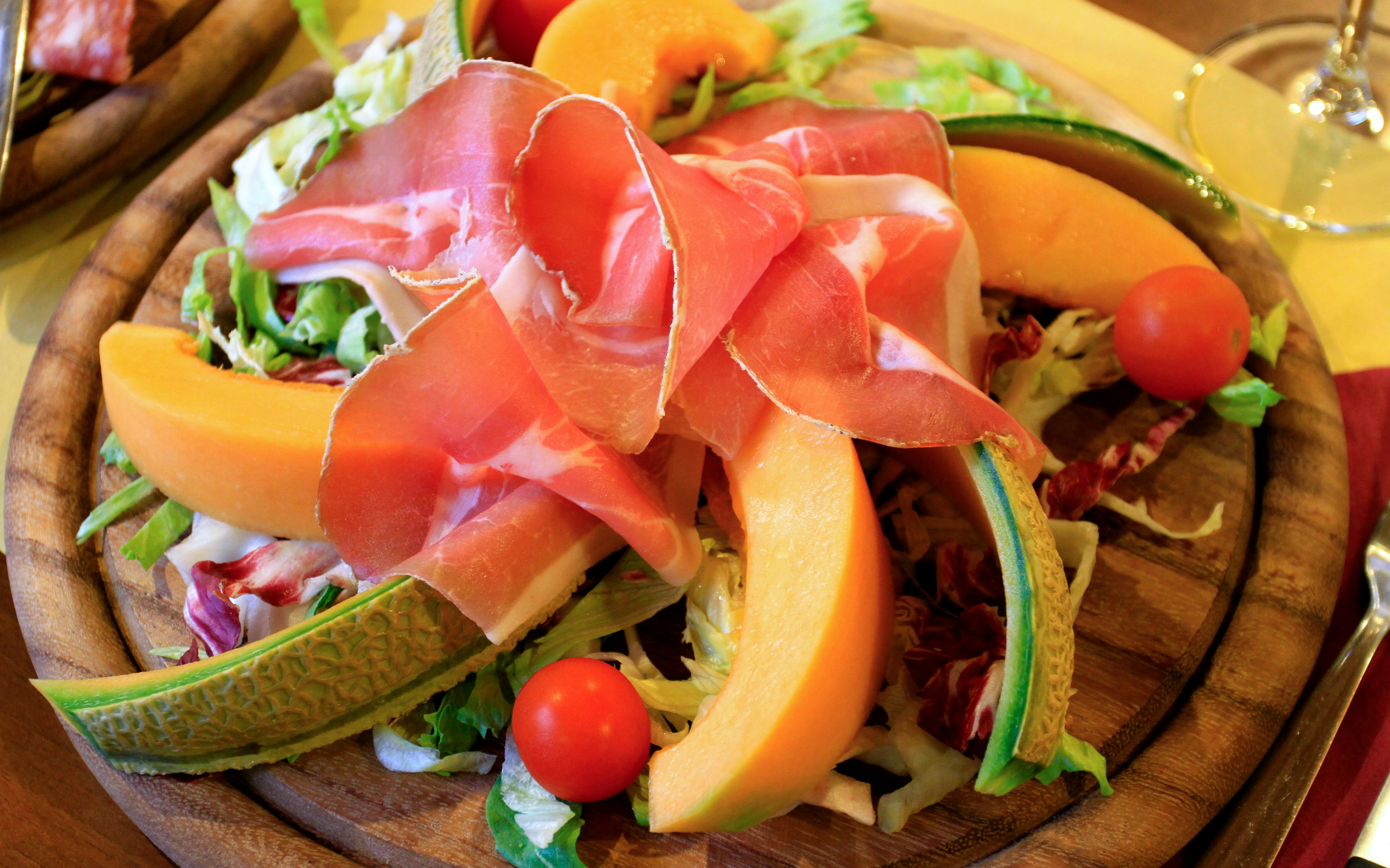 Prosciutto e melone with cherry tomatoes and lettuce on a wooden plate.