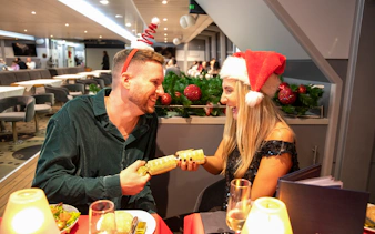 Guests enjoying Christmas dinner on Thames River cruise with festive hats.