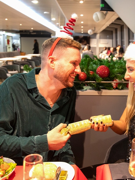 Guests enjoying Christmas dinner on Thames River cruise with festive hats.