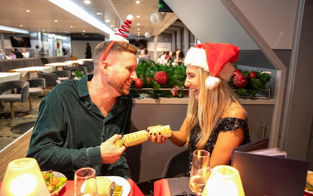 Guests enjoying Christmas dinner on Thames River cruise with festive hats.