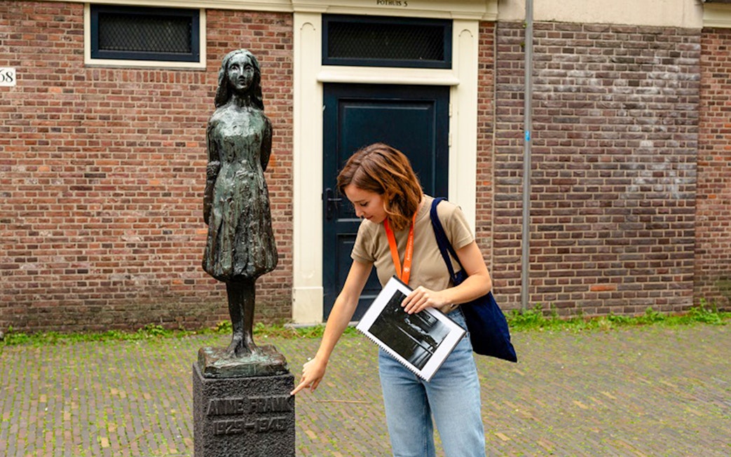 Tour guide pointing at Anne Frank statue in Amsterdam.
