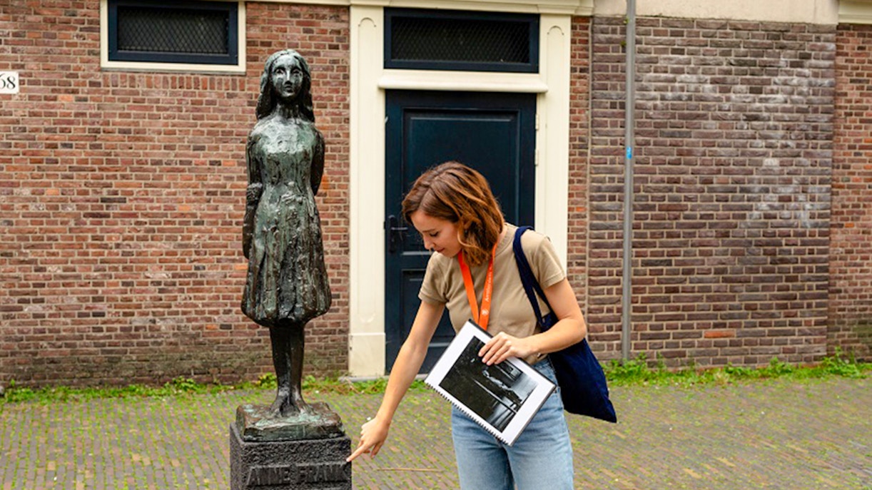 Tour guide pointing at Anne Frank statue in Amsterdam.
