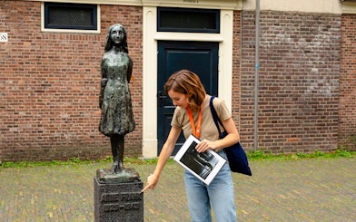 Tour guide pointing at Anne Frank statue in Amsterdam.