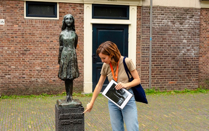 Tour guide pointing at Anne Frank statue in Amsterdam.