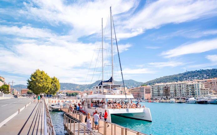 Catamaran docked at Villefranche bay with passengers boarding for snorkeling cruise.