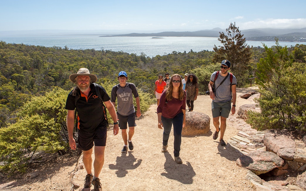Group hiking on a trail with views of Wineglass Bay, Tasmania.