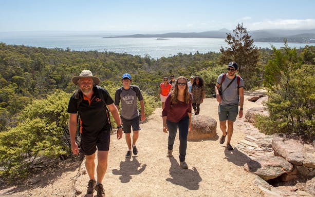 Group hiking on a trail with views of Wineglass Bay, Tasmania.